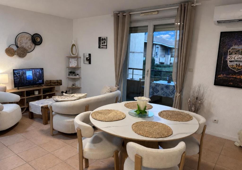 Séjour du Castelli : table ronde en marbre blanc et chaises crème, baie vitrée ouverte sur la terrasse couverte