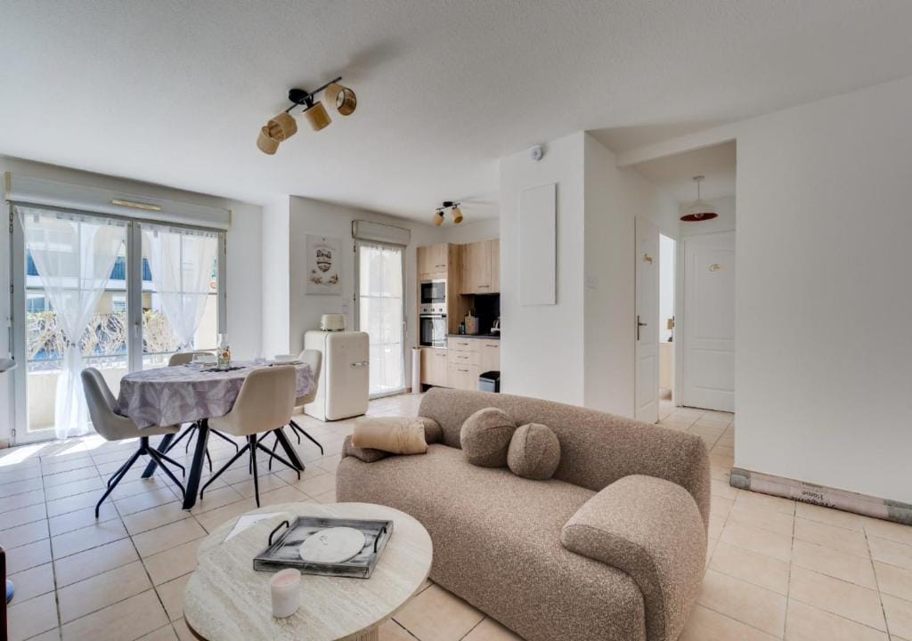 Pièce de vie du Marco : canapé bouclette beige, table ronde, cuisine équipée en bois clair au fond