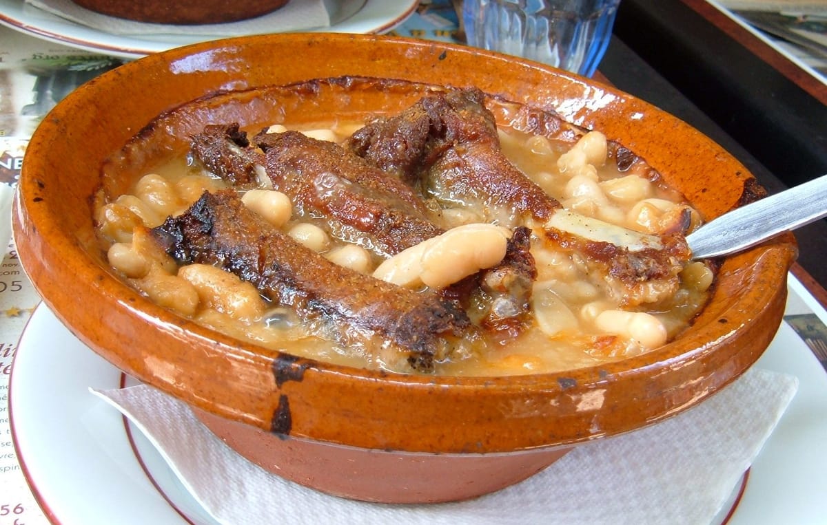 Un cassoulet servi dans sa cassole en terre cuite, haricots blancs et saucisse